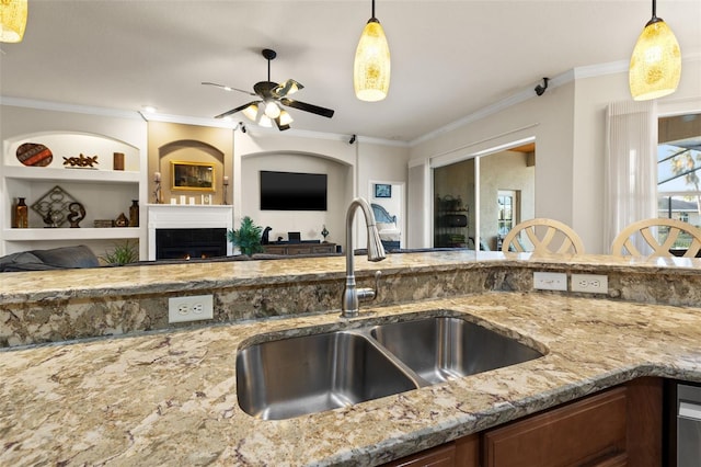 kitchen with sink, decorative light fixtures, ornamental molding, built in features, and a tiled fireplace