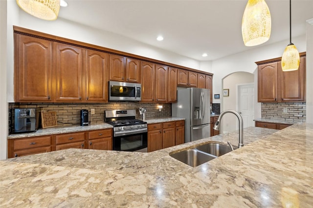 kitchen featuring sink, light stone counters, decorative light fixtures, stainless steel appliances, and decorative backsplash