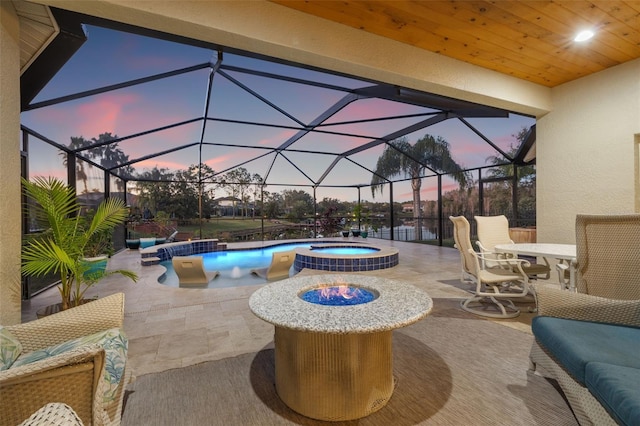 pool at dusk with an in ground hot tub, a lanai, pool water feature, and a patio