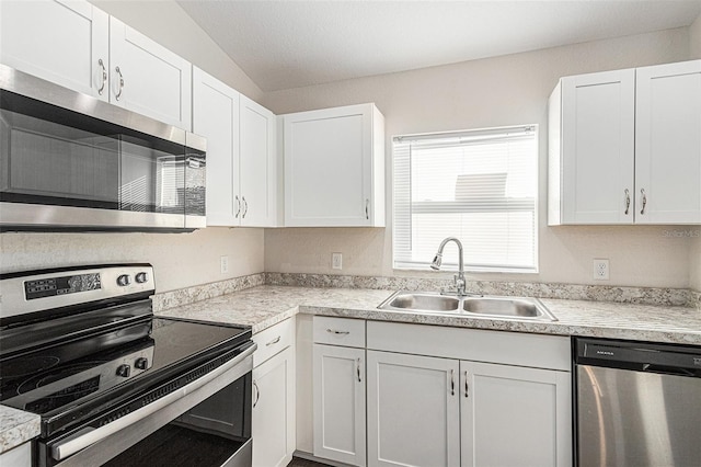 kitchen featuring white cabinets, appliances with stainless steel finishes, vaulted ceiling, and sink