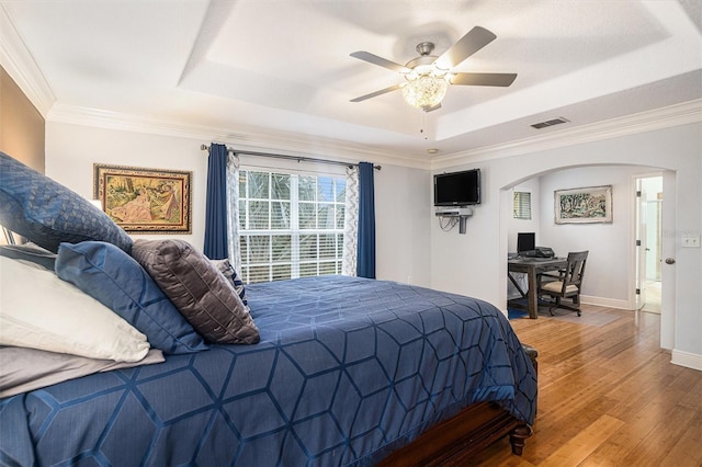 bedroom featuring ceiling fan, a raised ceiling, wood-type flooring, and crown molding