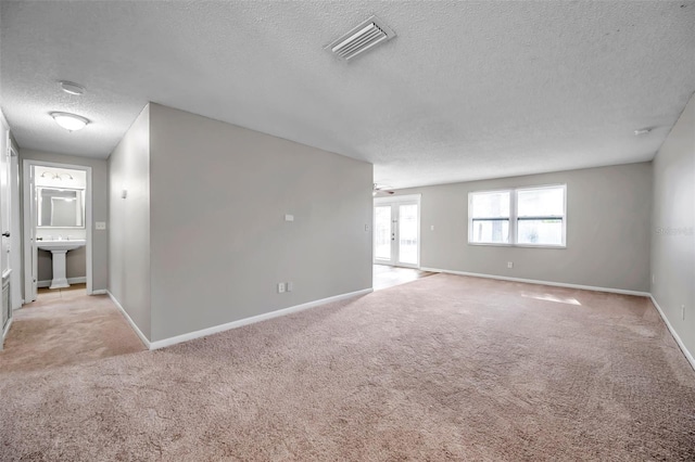 carpeted empty room with a textured ceiling, french doors, and sink