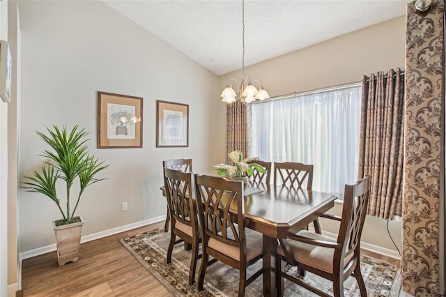 dining space featuring hardwood / wood-style flooring, a textured ceiling, lofted ceiling, and a chandelier