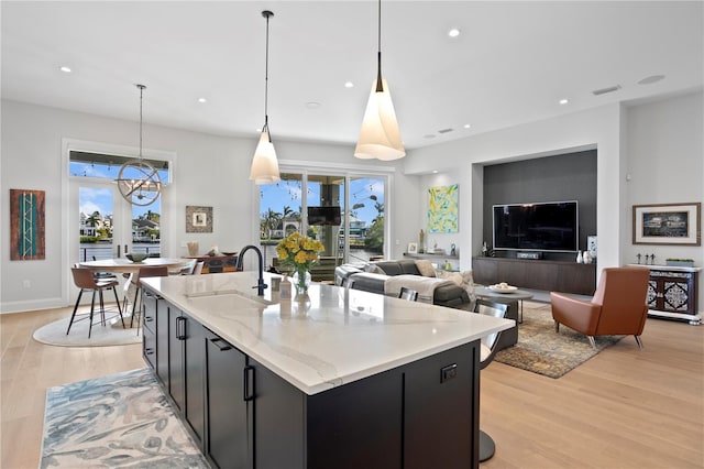 kitchen featuring a kitchen island with sink, sink, decorative light fixtures, and a notable chandelier