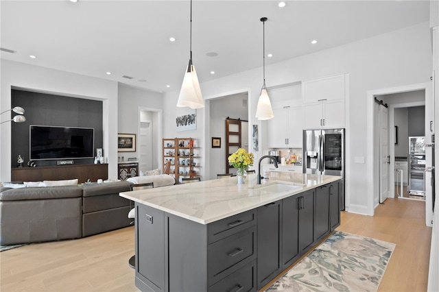 kitchen with light stone counters, pendant lighting, a barn door, white cabinets, and an island with sink