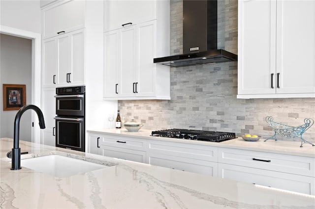 kitchen featuring light stone countertops, backsplash, sink, black appliances, and wall chimney range hood