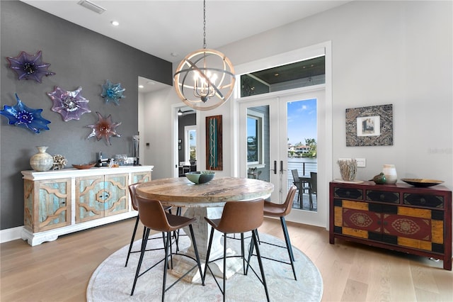 dining space with french doors, light wood-type flooring, and an inviting chandelier