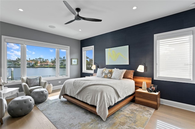 bedroom with ceiling fan, a water view, and light hardwood / wood-style floors