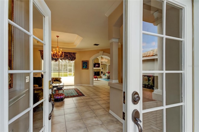 interior space with french doors, a raised ceiling, a notable chandelier, light tile patterned flooring, and ornamental molding