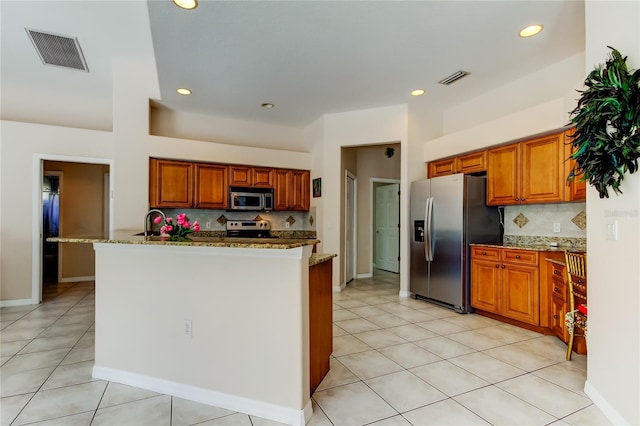 kitchen with stainless steel appliances, tasteful backsplash, light stone counters, a kitchen island with sink, and light tile patterned floors