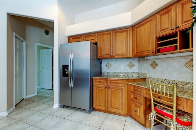 kitchen featuring light stone countertops, stainless steel fridge, decorative backsplash, and light tile patterned flooring