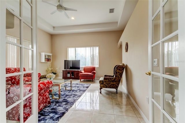 living room with light tile patterned floors, a tray ceiling, and ceiling fan