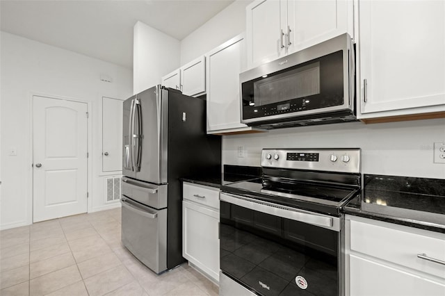 kitchen featuring light tile patterned floors, dark stone counters, stainless steel appliances, and white cabinetry