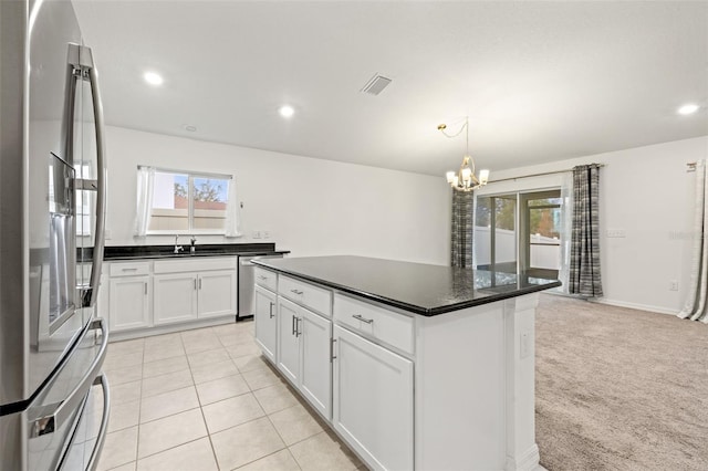 kitchen with white cabinets, appliances with stainless steel finishes, a kitchen island, light carpet, and a chandelier