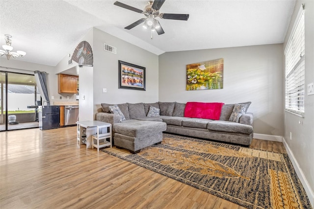 living room with ceiling fan with notable chandelier, light hardwood / wood-style floors, lofted ceiling, and a textured ceiling