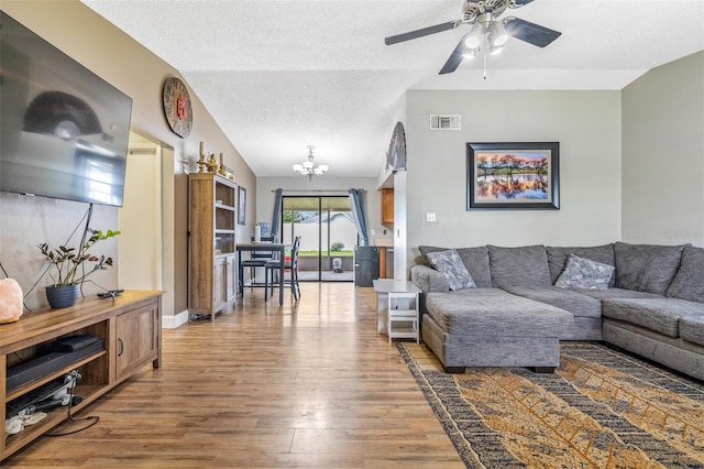 living room featuring a textured ceiling, ceiling fan with notable chandelier, wood-type flooring, and lofted ceiling