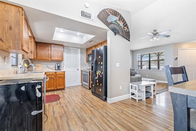 kitchen with ceiling fan, sink, light hardwood / wood-style floors, a tray ceiling, and black appliances