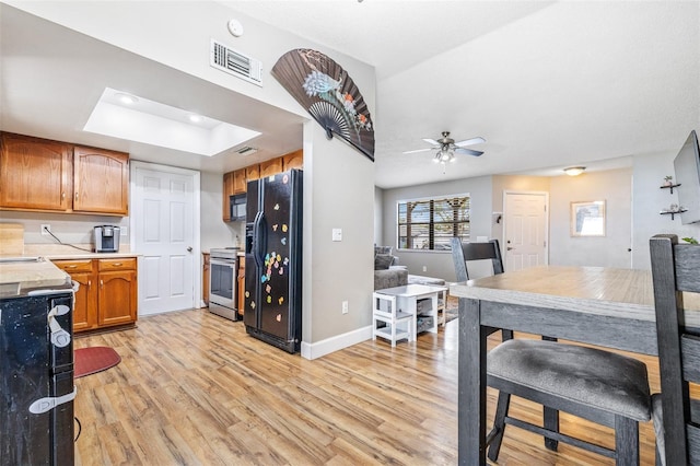 kitchen featuring black appliances, ceiling fan, a tray ceiling, and light hardwood / wood-style flooring