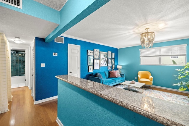 living room with crown molding, a textured ceiling, wood-type flooring, a chandelier, and a healthy amount of sunlight