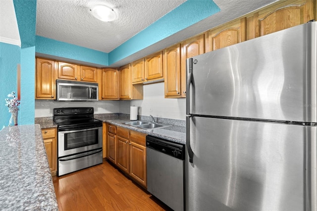 kitchen with appliances with stainless steel finishes, a textured ceiling, sink, dark stone countertops, and dark hardwood / wood-style flooring