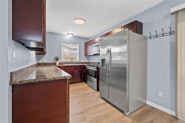 kitchen featuring light hardwood / wood-style floors, stainless steel appliances, dark stone countertops, and sink