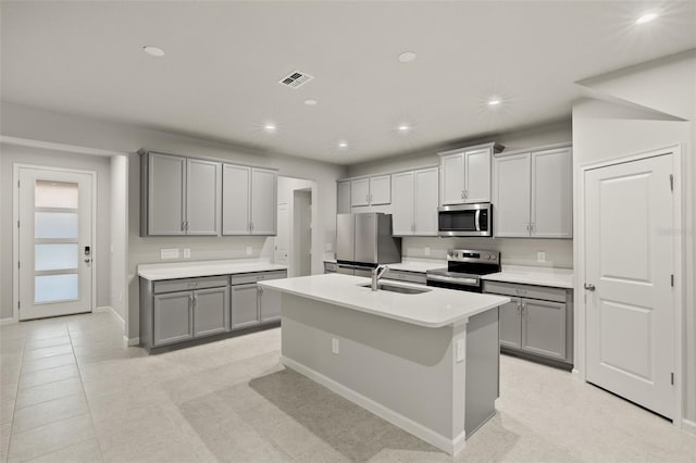 kitchen featuring a kitchen island with sink, sink, gray cabinetry, and appliances with stainless steel finishes