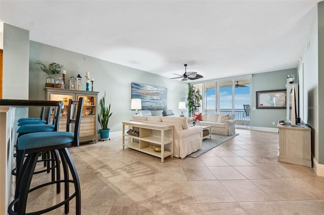 living area with light tile patterned floors, a wall of windows, a ceiling fan, and baseboards