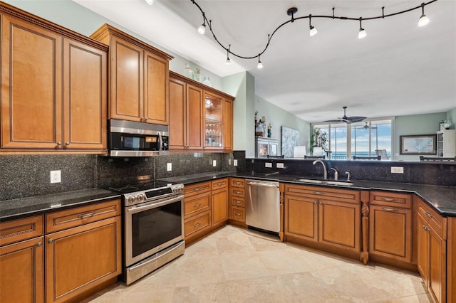 kitchen with brown cabinetry, dark stone countertops, a sink, stainless steel appliances, and backsplash