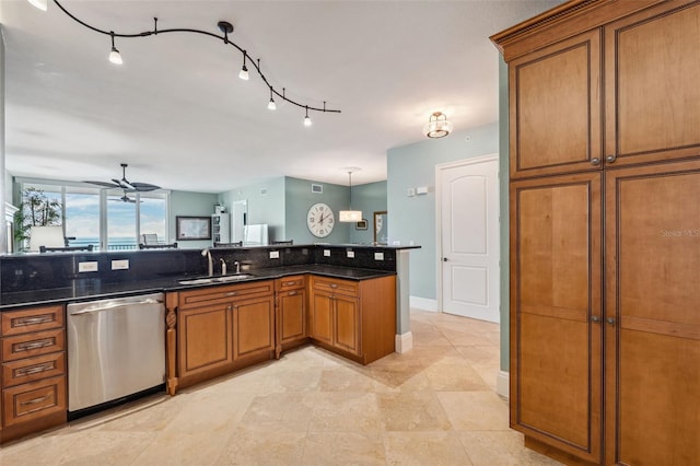 kitchen with brown cabinets, stainless steel dishwasher, a sink, ceiling fan, and dark stone countertops