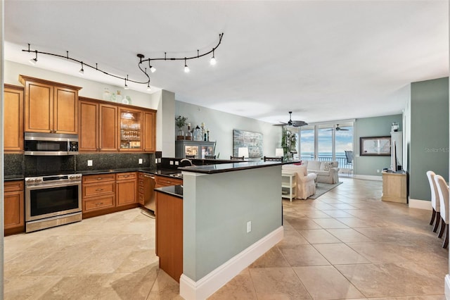 kitchen featuring tasteful backsplash, brown cabinetry, dark countertops, appliances with stainless steel finishes, and open floor plan