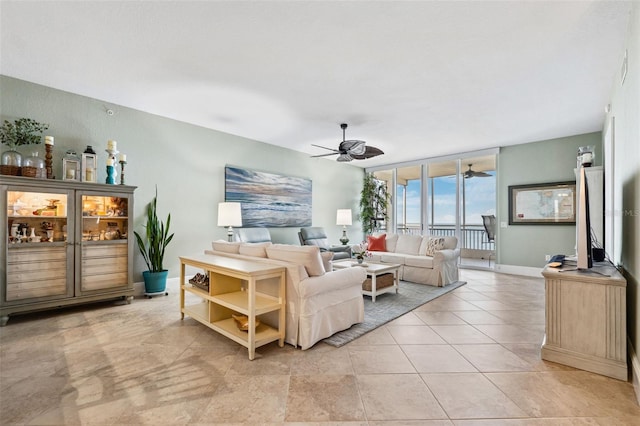 living room featuring light tile patterned floors, ceiling fan, baseboards, and a wall of windows