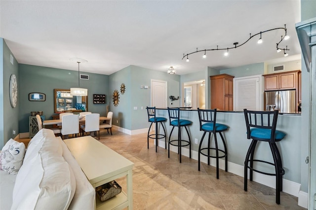 kitchen featuring brown cabinets, visible vents, stainless steel refrigerator with ice dispenser, and a breakfast bar area