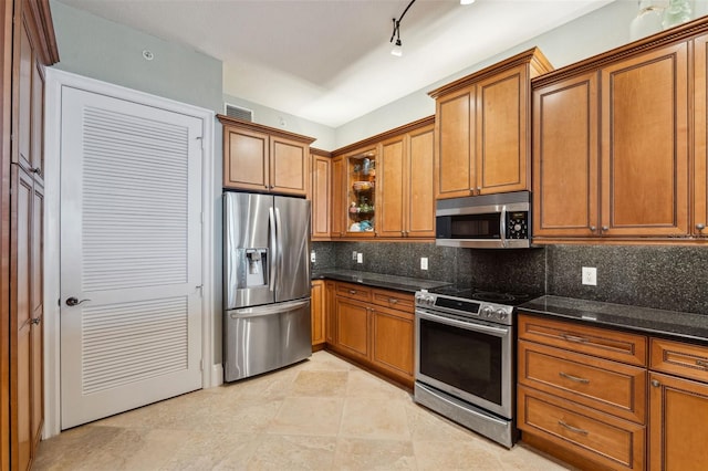 kitchen with stainless steel appliances, brown cabinets, dark stone counters, tasteful backsplash, and glass insert cabinets