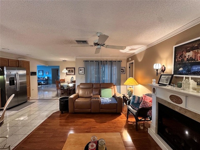 living room featuring a textured ceiling, ceiling fan, ornamental molding, and light tile patterned flooring