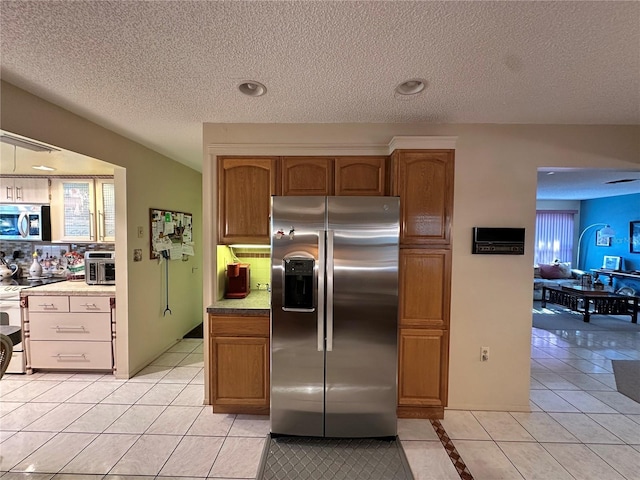 kitchen with appliances with stainless steel finishes, backsplash, a textured ceiling, and light tile patterned floors