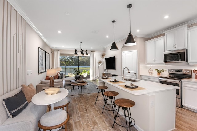 kitchen featuring a kitchen island with sink, white cabinets, hanging light fixtures, sink, and appliances with stainless steel finishes