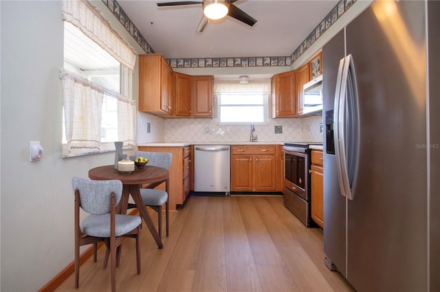 kitchen with sink, light hardwood / wood-style flooring, ceiling fan, stainless steel appliances, and decorative backsplash