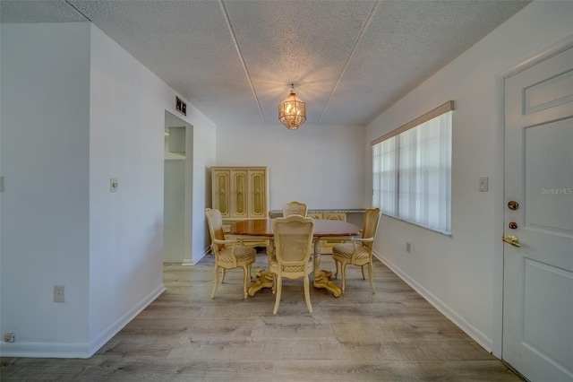 dining area with a textured ceiling, a notable chandelier, and light hardwood / wood-style flooring