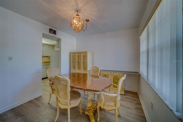 dining space with a textured ceiling, light hardwood / wood-style flooring, and an inviting chandelier