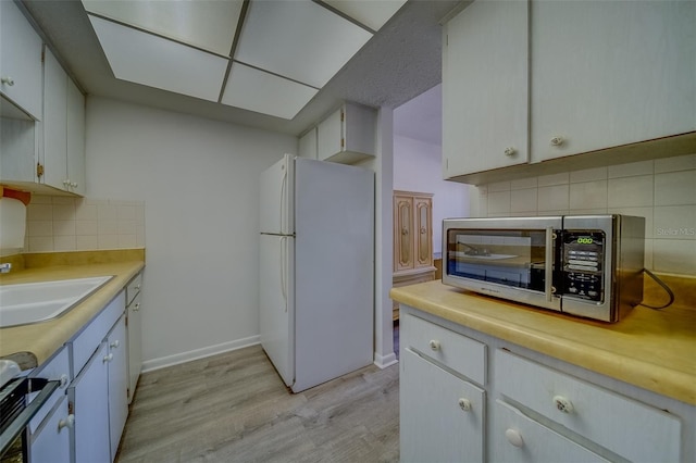 kitchen featuring sink, white cabinetry, white appliances, tasteful backsplash, and light hardwood / wood-style flooring