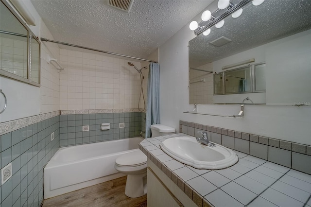 full bathroom featuring a textured ceiling, tile walls, hardwood / wood-style floors, toilet, and tiled shower / bath combo