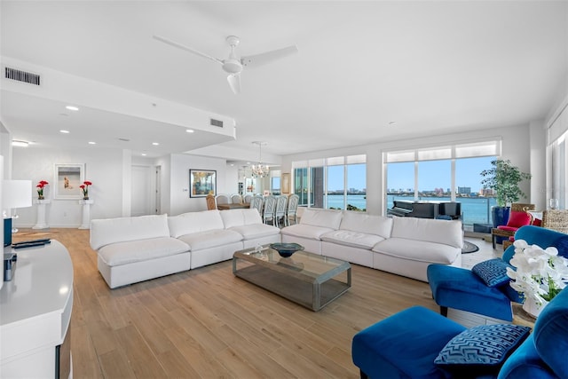 living room featuring a water view, light wood-type flooring, and ceiling fan with notable chandelier