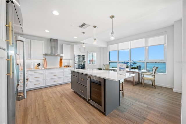 kitchen featuring wine cooler, pendant lighting, white cabinetry, a water view, and wall chimney exhaust hood