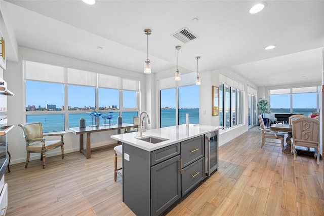 kitchen with gray cabinetry, decorative light fixtures, a kitchen island with sink, beverage cooler, and sink