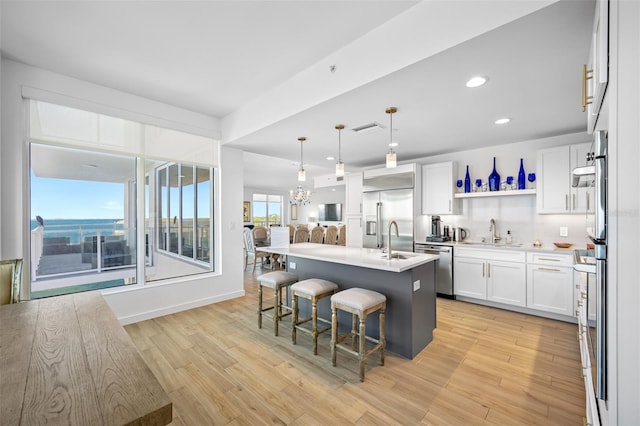 kitchen with a kitchen bar, an island with sink, white cabinetry, and stainless steel appliances