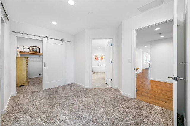 unfurnished bedroom with a closet, light colored carpet, and a barn door