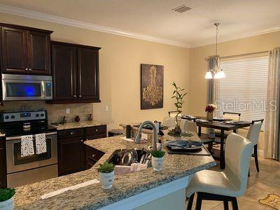 kitchen featuring light stone countertops, dark brown cabinets, stainless steel appliances, an inviting chandelier, and a breakfast bar area