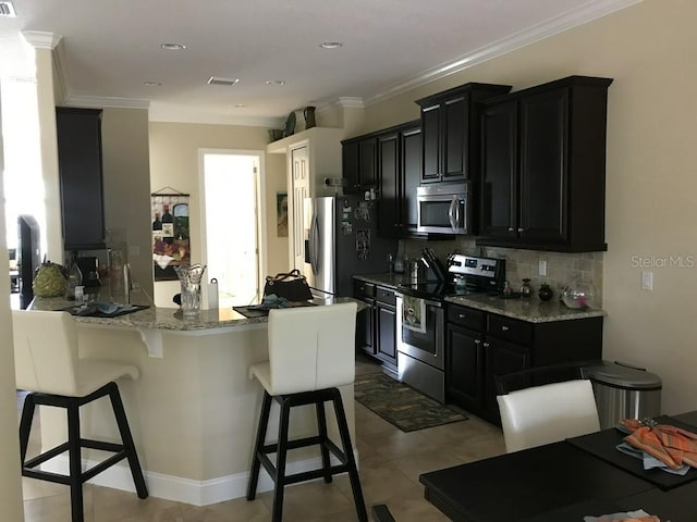 kitchen featuring decorative backsplash, appliances with stainless steel finishes, light stone countertops, a breakfast bar, and crown molding