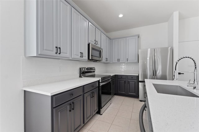 kitchen with appliances with stainless steel finishes, gray cabinets, light tile patterned floors, and sink