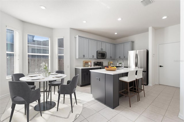 kitchen featuring sink, an island with sink, gray cabinets, light tile patterned floors, and appliances with stainless steel finishes